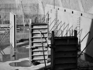 Construction site with wooden formwork and metal rebar for concrete columns in a wet foundation area.